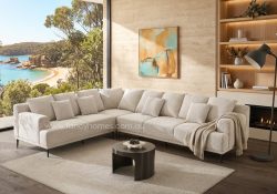 Renova modern corner fabric lounge suite in light beige upholstery with black metal legs, styled in a coastal living room.